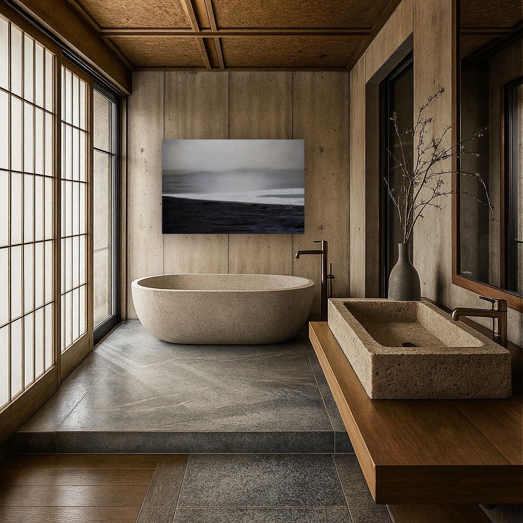 A minimalist bathroom with a freestanding bathtub and a wall-mounted sink, featuring a black and white artwork above the bathtub and a large window allowing natural light to fill the space.
