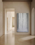 A abstract mixed media artwork on canvas titled 'Luminous Lines On Grey', displayed in a bright hallway with light streaming in from the windows.