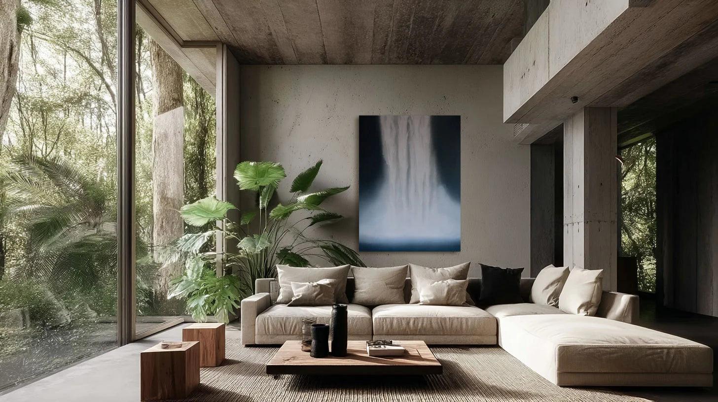 A modern living room with a large abstract painting in shades of blue and white, surrounded by floor-to-ceiling windows with a view of greenery outside. The room features a neutral color scheme with wooden elements and a cozy sofa setup.