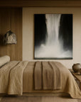 A minimalist bedroom with a large bed, wooden headboard, and beige bedding. The room features a prominent black and white artwork hanging above the bed, with decorative bowls and a wooden bench complementing the earthy tones.