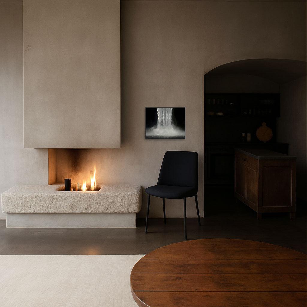 A framed artwork titled 'Black Lines' hanging on a wall above a modern fireplace in a stylishly decorated room with a chair and round wooden table.