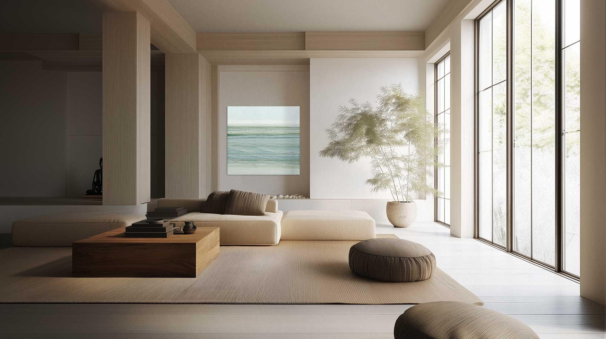 A serene and minimalist living room with a large window, a white sofa, armchairs, and a low coffee table. The wall features a print of a calm beach scene.