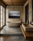 A minimalist bathroom with a freestanding bathtub and a wall-mounted sink, featuring a black and white artwork above the bathtub and a large window allowing natural light to fill the space.