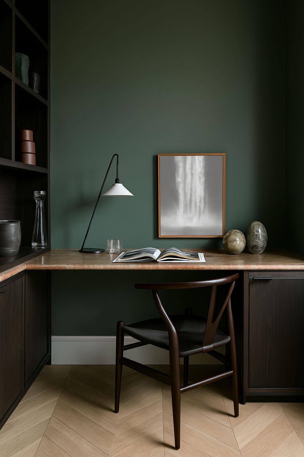 A framed artwork titled 'Eternally Falling Lines' displayed on a wooden desk with a lamp and a chair in a room with green walls.