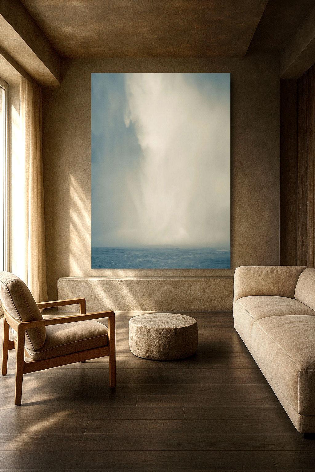 A large, minimalist artwork depicting a serene sky and sea scene, displayed on a wall in a well-lit living room setting with a sofa and armchair.
