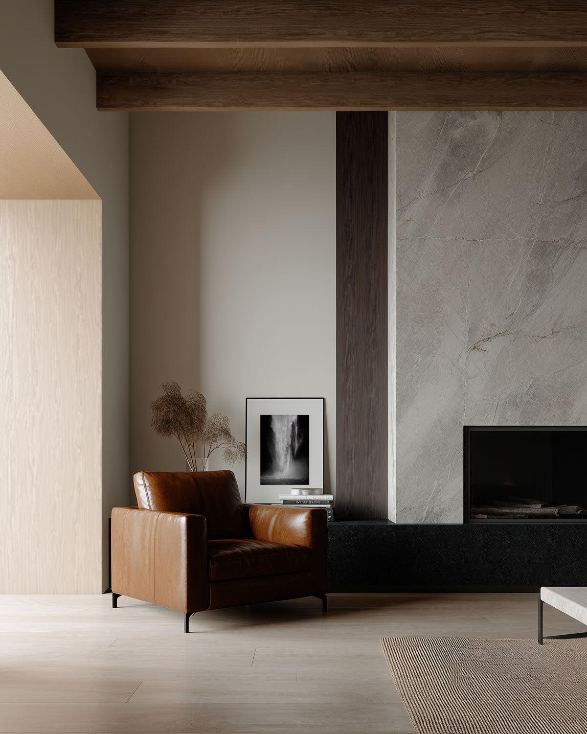 A minimalist interior featuring a modern armchair and a side table with a framed artwork above, set against a neutral-toned wall with a marble fireplace.