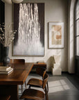 A painting titled 'Liberated Lines' featuring abstract white lines on a dark background, displayed on a wall above a wooden dining table and chairs.