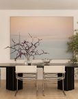 A dining room with a large painting of pink clouds.